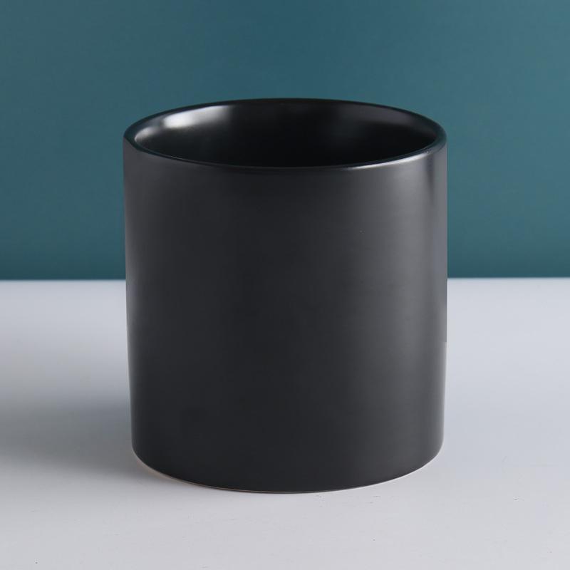 black cylinder pot placed on top of white table with teal background - Plant Studio