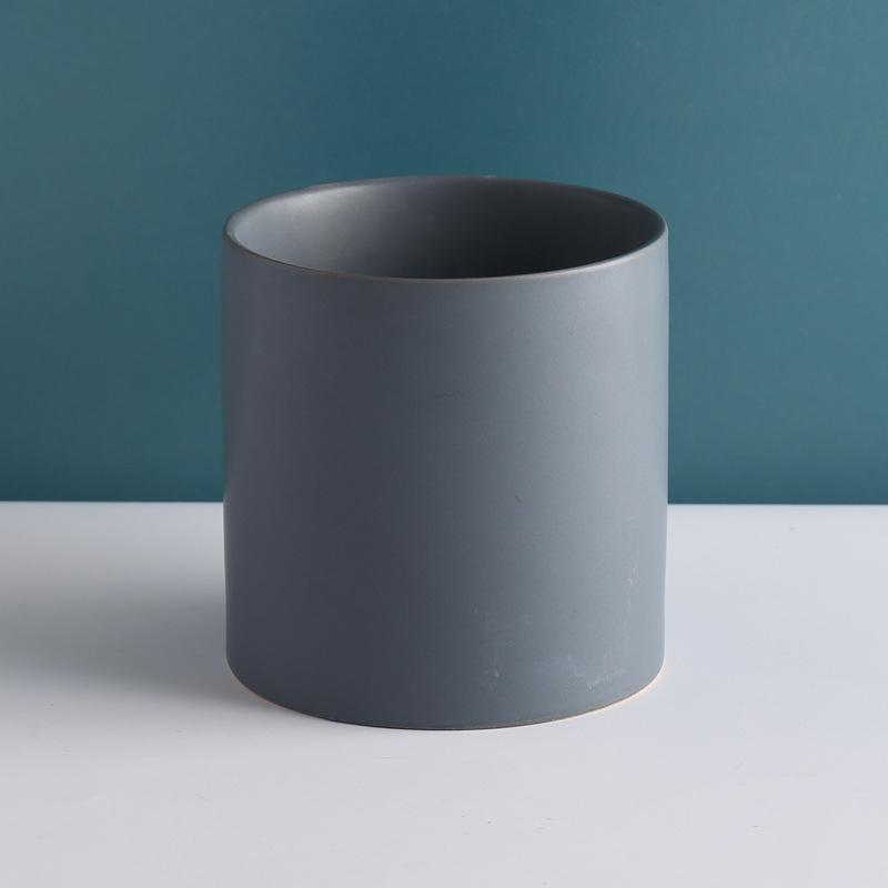 gray cylinder pot placed on top of white table with teal background - Plant Studio