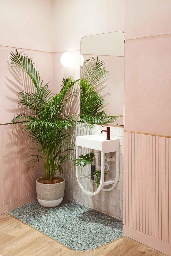 Areca Palm plant in beige and gray pot placed in bathroom with peach paint and white sink 